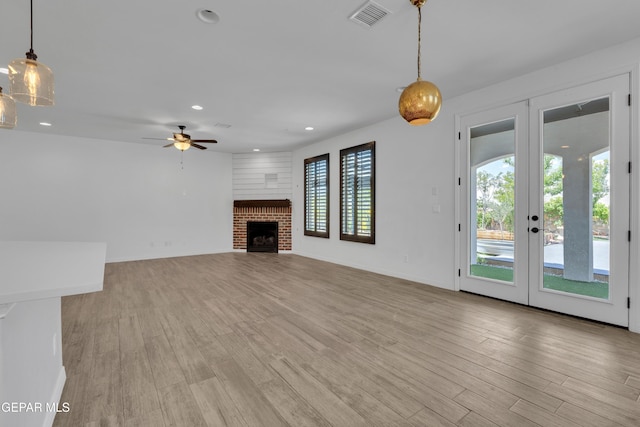 unfurnished living room with ceiling fan, light wood finished floors, recessed lighting, a brick fireplace, and french doors