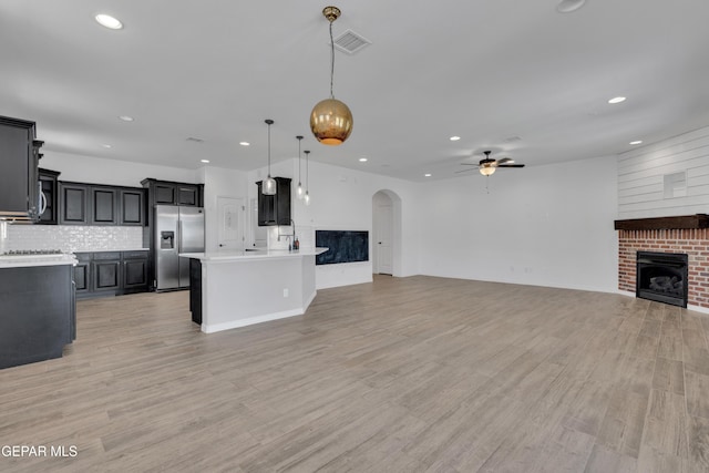 kitchen with stainless steel refrigerator with ice dispenser, open floor plan, a brick fireplace, a ceiling fan, and recessed lighting