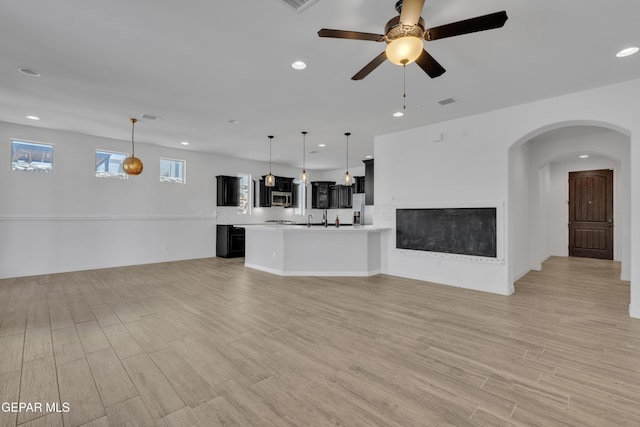 unfurnished living room featuring ceiling fan, recessed lighting, light wood finished floors, a fireplace, and arched walkways