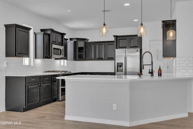 kitchen with appliances with stainless steel finishes, decorative backsplash, light wood-style flooring, light countertops, and pendant lighting