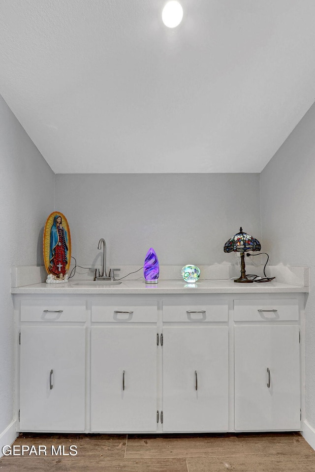 bar area with baseboards, a sink, and light wood-style flooring