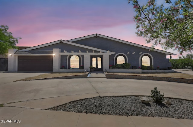 ranch-style home featuring driveway, brick siding, a garage, and french doors