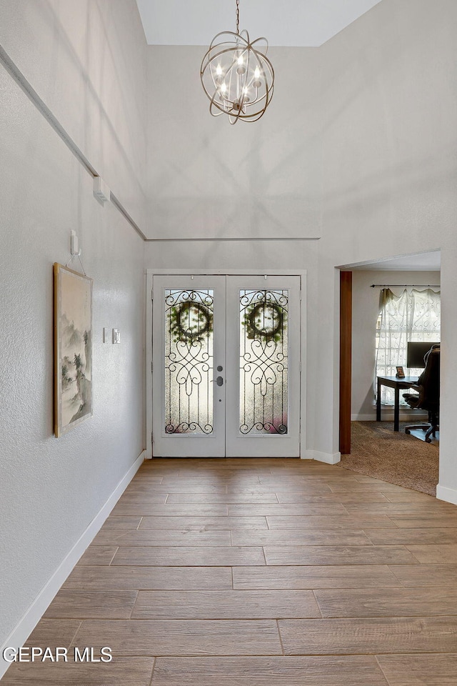 foyer featuring healthy amount of natural light, a chandelier, a high ceiling, french doors, and wood finished floors
