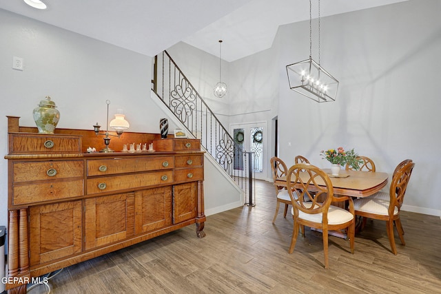 dining area with stairway, baseboards, light wood-style flooring, a chandelier, and a high ceiling