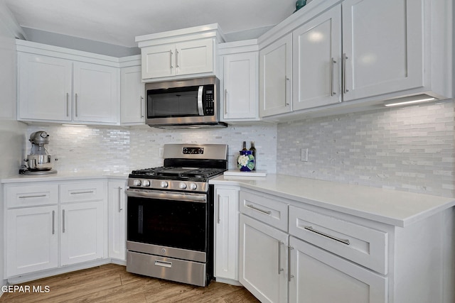 kitchen with appliances with stainless steel finishes, white cabinetry, light countertops, light wood-type flooring, and backsplash