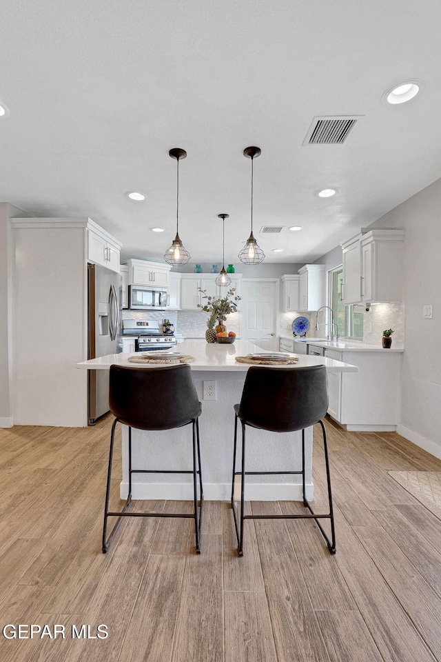 kitchen with stainless steel appliances, light countertops, light wood finished floors, white cabinetry, and recessed lighting