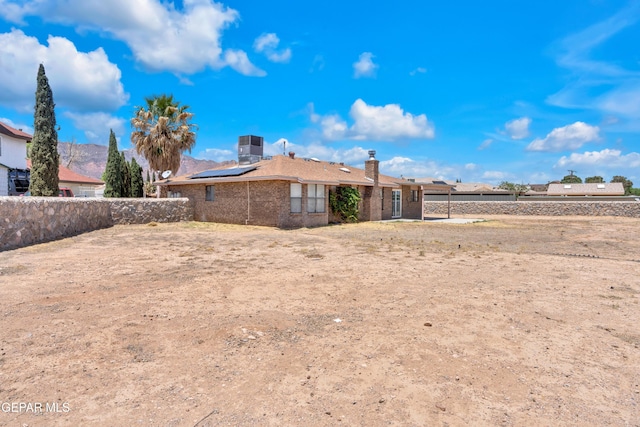 rear view of property with solar panels, fence, brick siding, a chimney, and central AC