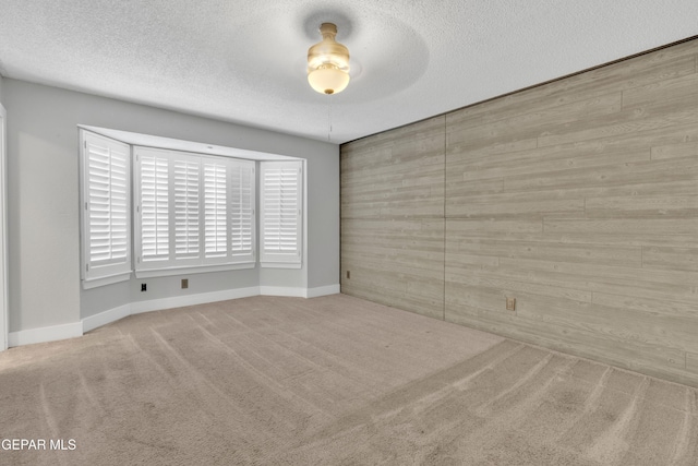 carpeted spare room featuring a textured ceiling and baseboards