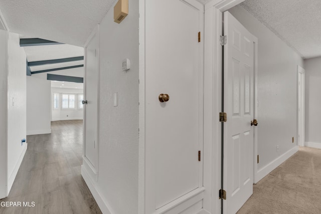 hall with a textured ceiling, baseboards, and light wood-style floors