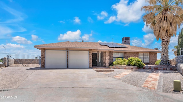 single story home with a garage, concrete driveway, a gate, roof mounted solar panels, and brick siding