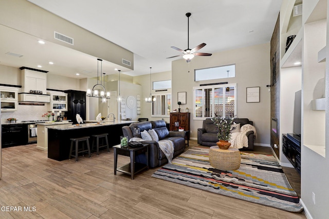 living area featuring a chandelier, a ceiling fan, light wood-type flooring, a high ceiling, and baseboards