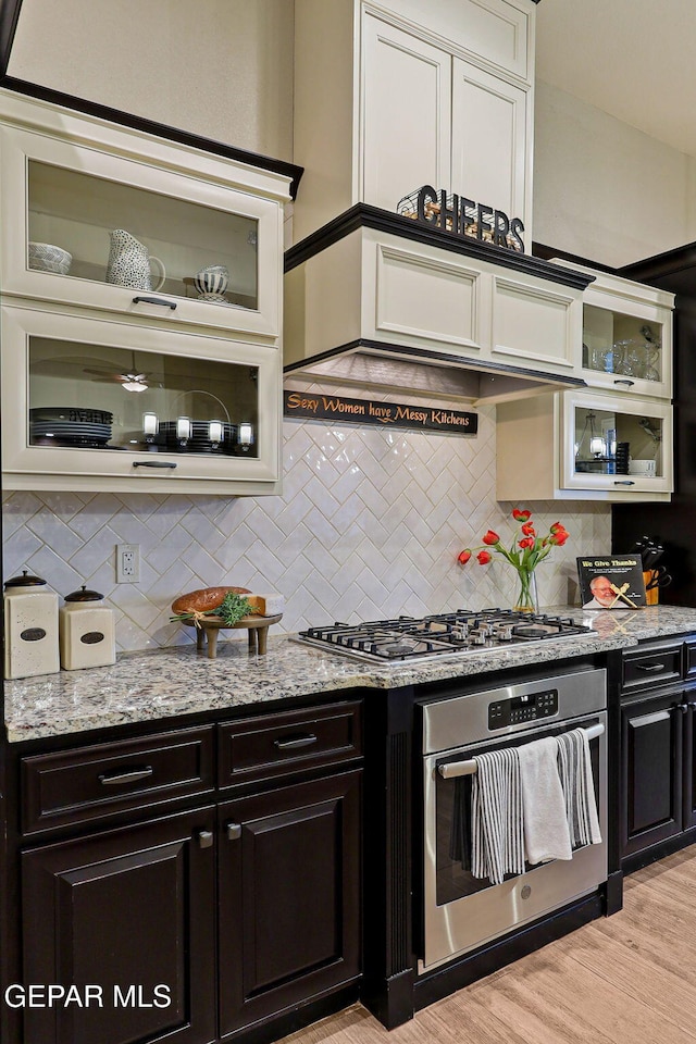 kitchen with stainless steel appliances, decorative backsplash, glass insert cabinets, and light stone counters