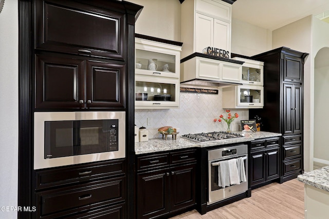 kitchen featuring appliances with stainless steel finishes, dark cabinetry, white cabinets, light wood-style flooring, and tasteful backsplash
