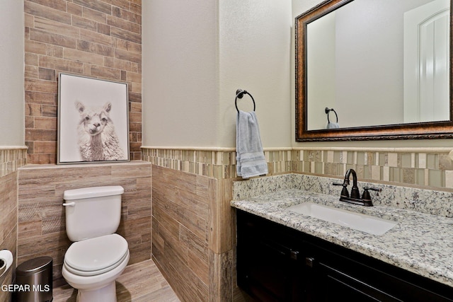 bathroom with tile walls, toilet, vanity, and wainscoting