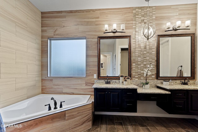 bathroom featuring a bath, double vanity, a chandelier, and wood finished floors