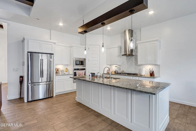 kitchen featuring appliances with stainless steel finishes, wall chimney range hood, a sink, backsplash, and recessed lighting