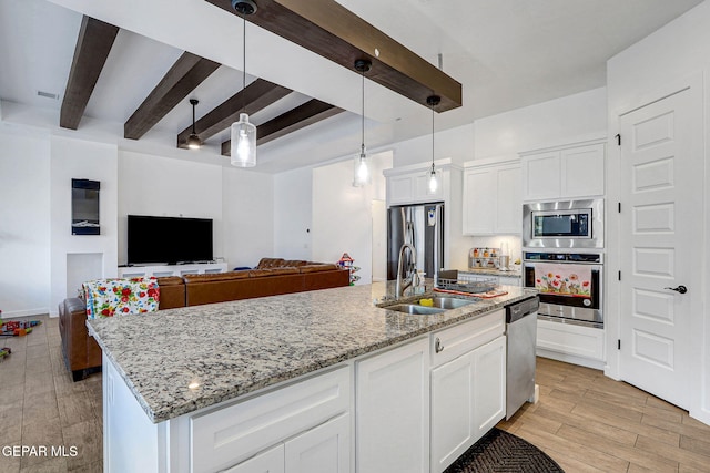 kitchen featuring stainless steel appliances, a sink, beam ceiling, light stone countertops, and white cabinets