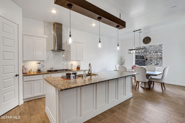 kitchen featuring wall chimney exhaust hood, stainless steel gas cooktop, white cabinetry, and backsplash