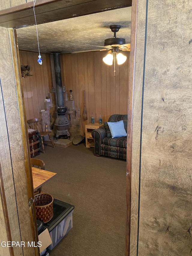 sitting room with wood walls, a wood stove, ceiling fan, and carpet flooring