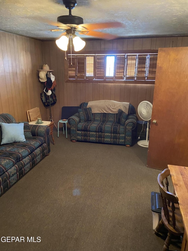 living room with ceiling fan, wooden walls, carpet flooring, and a textured ceiling