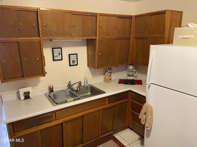 kitchen with freestanding refrigerator, a sink, light countertops, and light tile patterned flooring