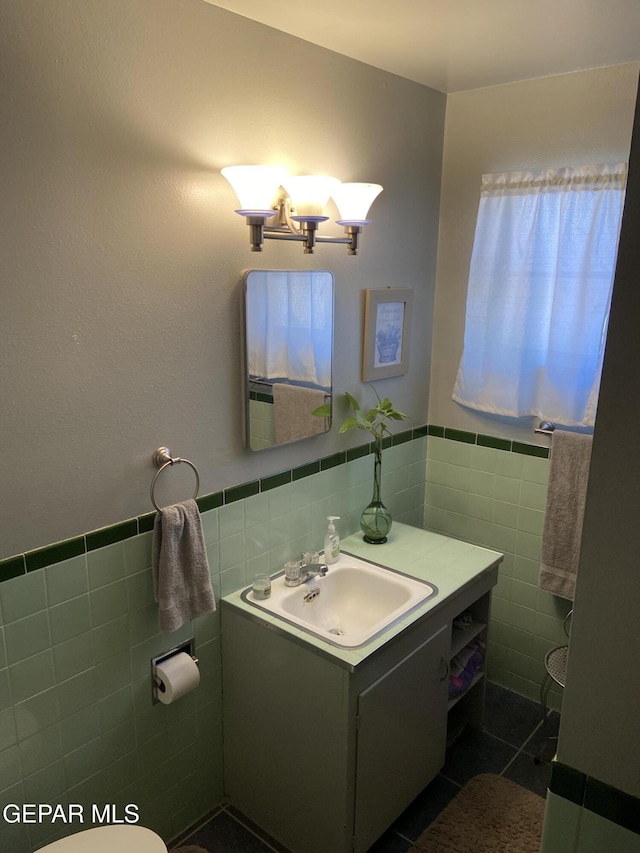 half bath with tile walls, vanity, a chandelier, a wainscoted wall, and tile patterned floors