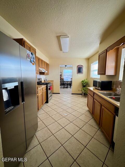 kitchen featuring stainless steel appliances, a sink, light tile patterned floors, a textured ceiling, and brown cabinets
