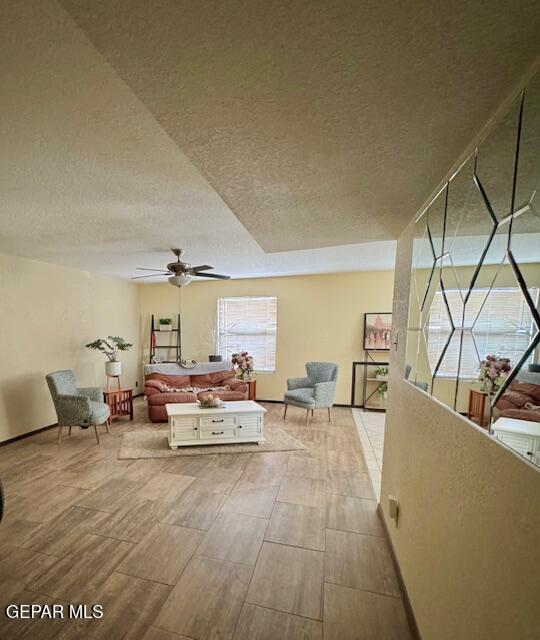 living room featuring a textured ceiling, wood finished floors, ceiling fan, and baseboards
