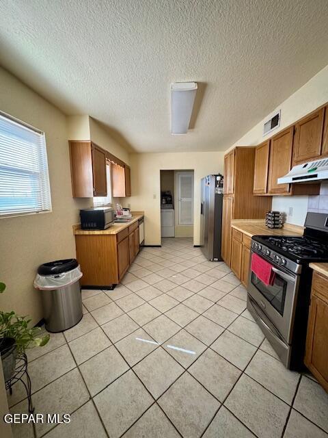 kitchen featuring stainless steel range with gas cooktop, under cabinet range hood, freestanding refrigerator, light countertops, and a textured ceiling
