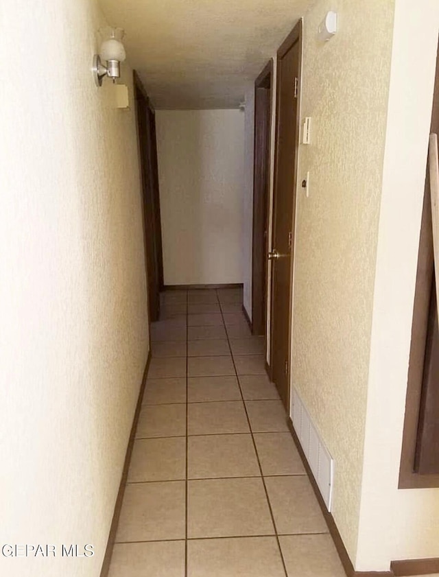 hallway featuring a textured wall and light tile patterned floors