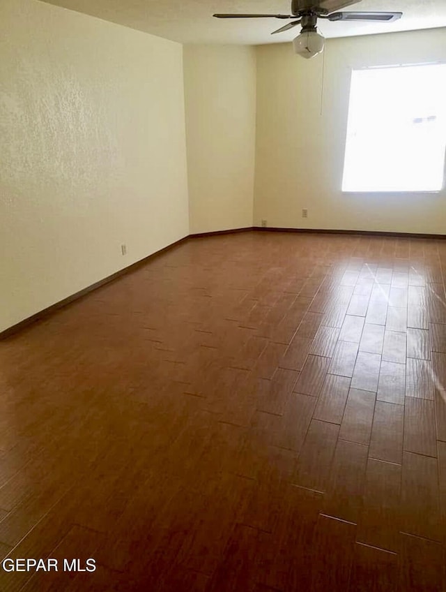 unfurnished room featuring a ceiling fan, baseboards, and dark wood-type flooring
