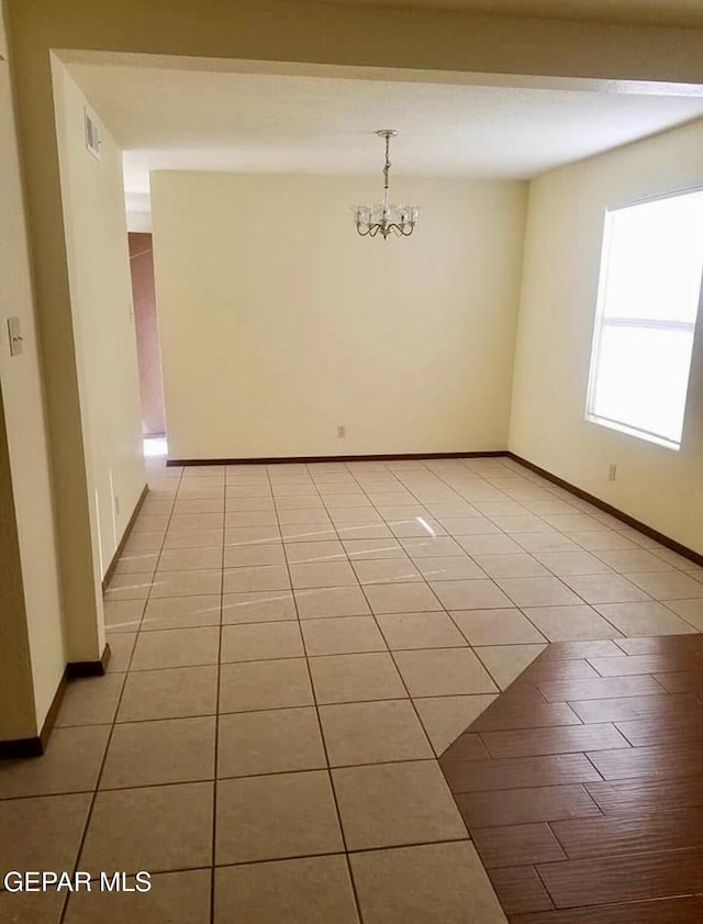 unfurnished room with light tile patterned floors, a chandelier, and baseboards