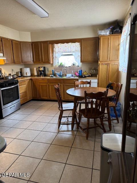 kitchen featuring stainless steel gas range oven, light tile patterned floors, brown cabinets, light countertops, and a textured ceiling