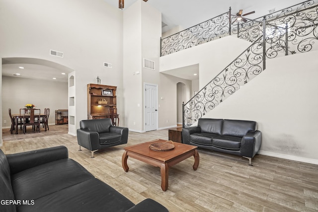living area with arched walkways, light wood finished floors, a towering ceiling, and baseboards
