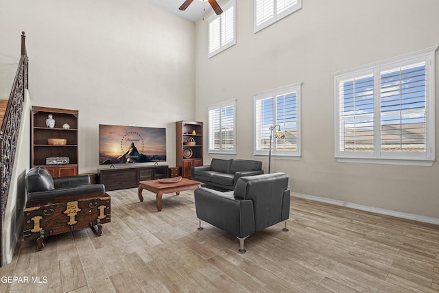 living room with ceiling fan, a towering ceiling, wood finished floors, and baseboards