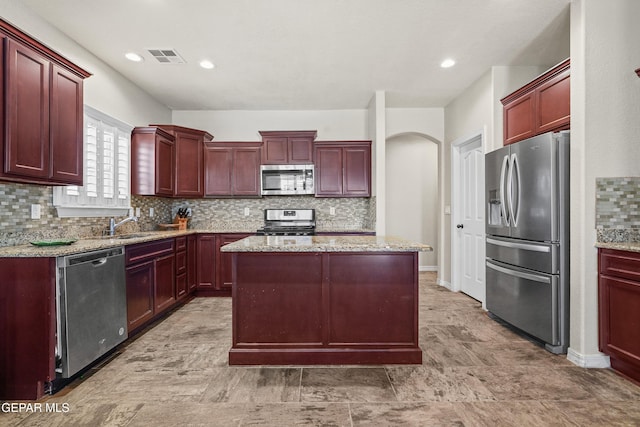kitchen with stainless steel appliances, dark brown cabinets, light stone countertops, and recessed lighting