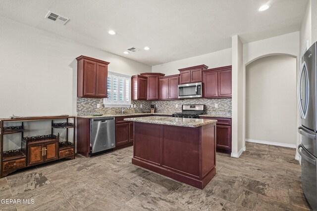 kitchen with appliances with stainless steel finishes, reddish brown cabinets, decorative backsplash, light stone counters, and arched walkways
