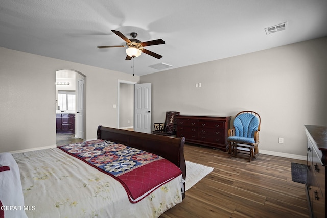 bedroom with wood finished floors, arched walkways, baseboards, a ceiling fan, and connected bathroom
