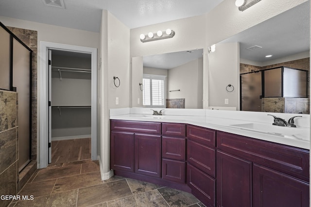full bath with a stall shower, double vanity, a walk in closet, and stone finish flooring