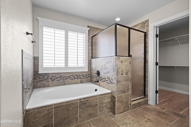 full bath featuring a shower stall, a spacious closet, and a garden tub