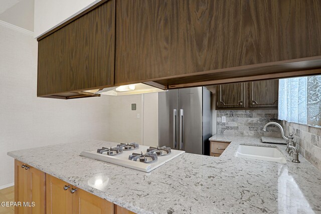 kitchen featuring freestanding refrigerator, a sink, white gas stovetop, light stone counters, and a peninsula