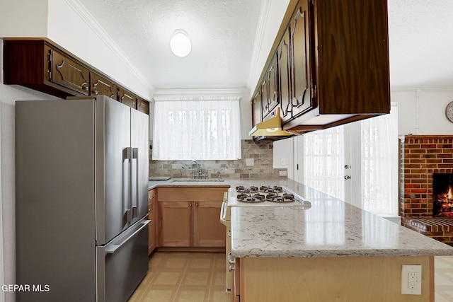 kitchen featuring freestanding refrigerator, a sink, light flooring, under cabinet range hood, and a fireplace