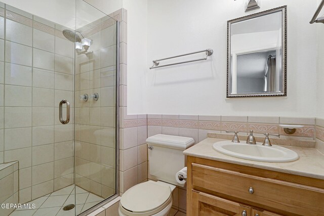 full bath featuring a shower stall, toilet, wainscoting, vanity, and tile walls