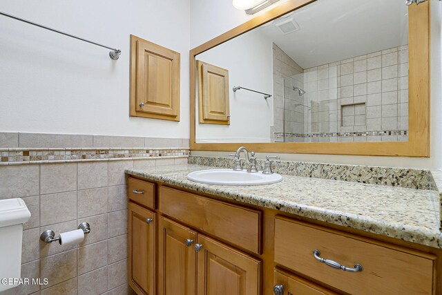 bathroom featuring vanity, toilet, tile walls, and tiled shower
