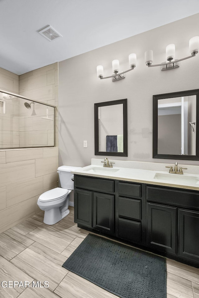 bathroom featuring toilet, double vanity, and tiled shower
