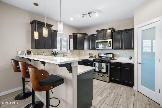 kitchen featuring appliances with stainless steel finishes, a kitchen bar, decorative backsplash, light countertops, and a peninsula