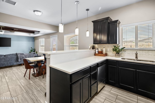 kitchen featuring a sink, dishwasher, open floor plan, a peninsula, and light countertops