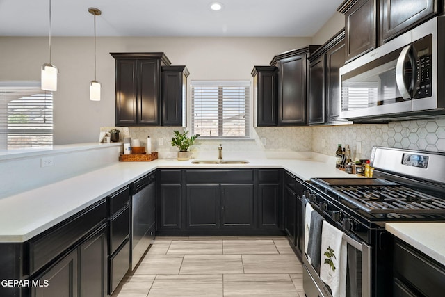 kitchen with appliances with stainless steel finishes, a sink, tasteful backsplash, light countertops, and a peninsula