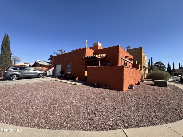 10620 Cuatro Vistas Dr Unit A, El Paso, TX 79935 - view of side of property featuring an attached garage, a chimney, stucco siding, and driveway