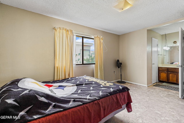 bedroom featuring a textured ceiling, ensuite bathroom, and baseboards